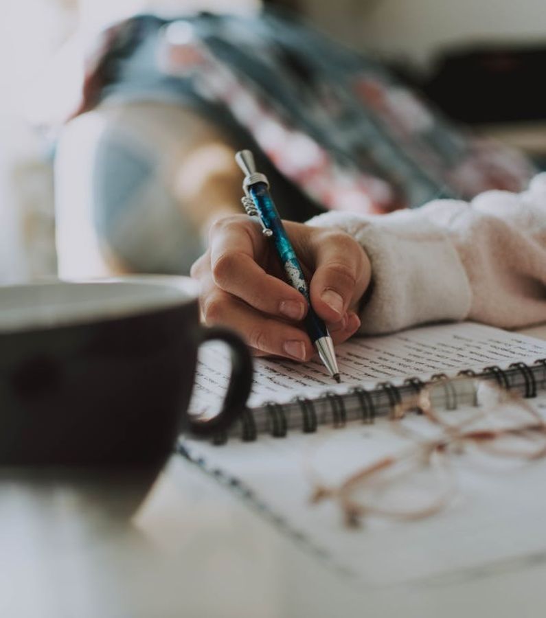 Copywriter writes in a notebook while a cup of coffee sits nearby
